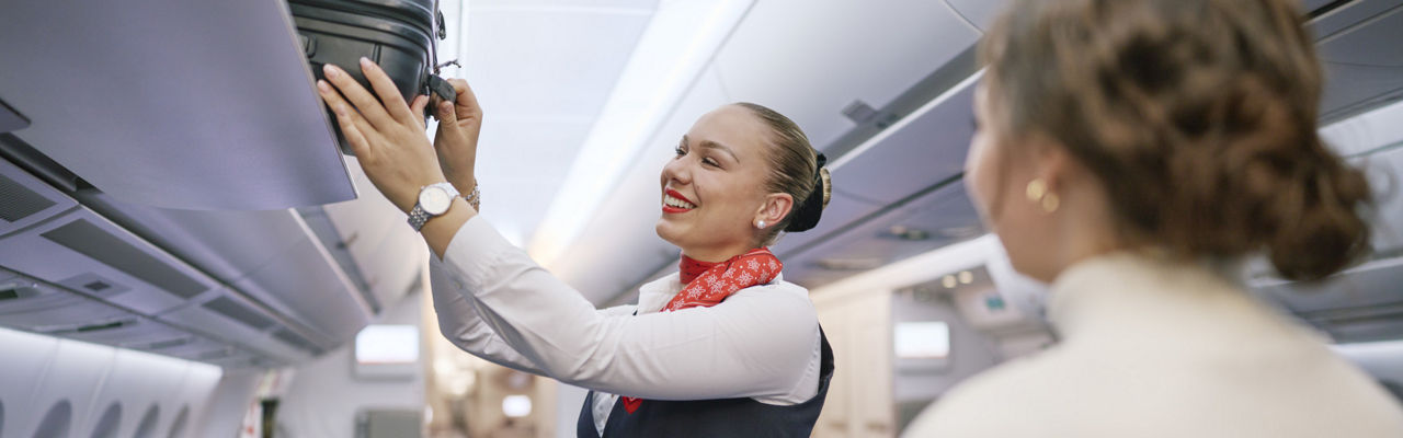 A crew member helps to stow a suitcase in the overhead compartment