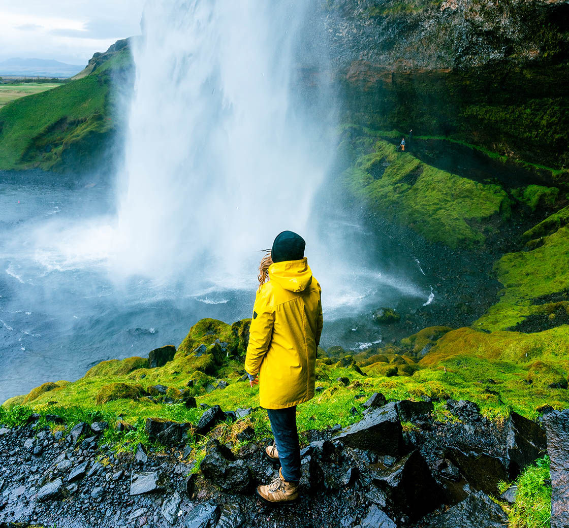 A person standing on a rocky cliff looking at a waterfall