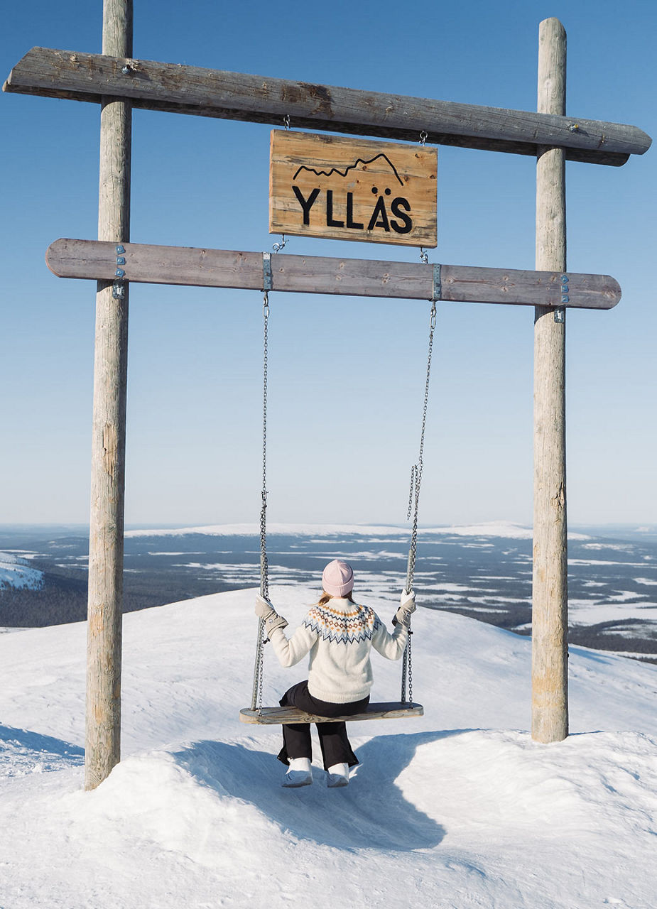 Frau auf einer Schaukel im Schnee unter Ylläs-Schild