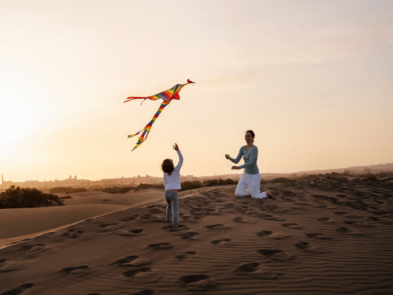 A woman and a child fly a kite in the sand