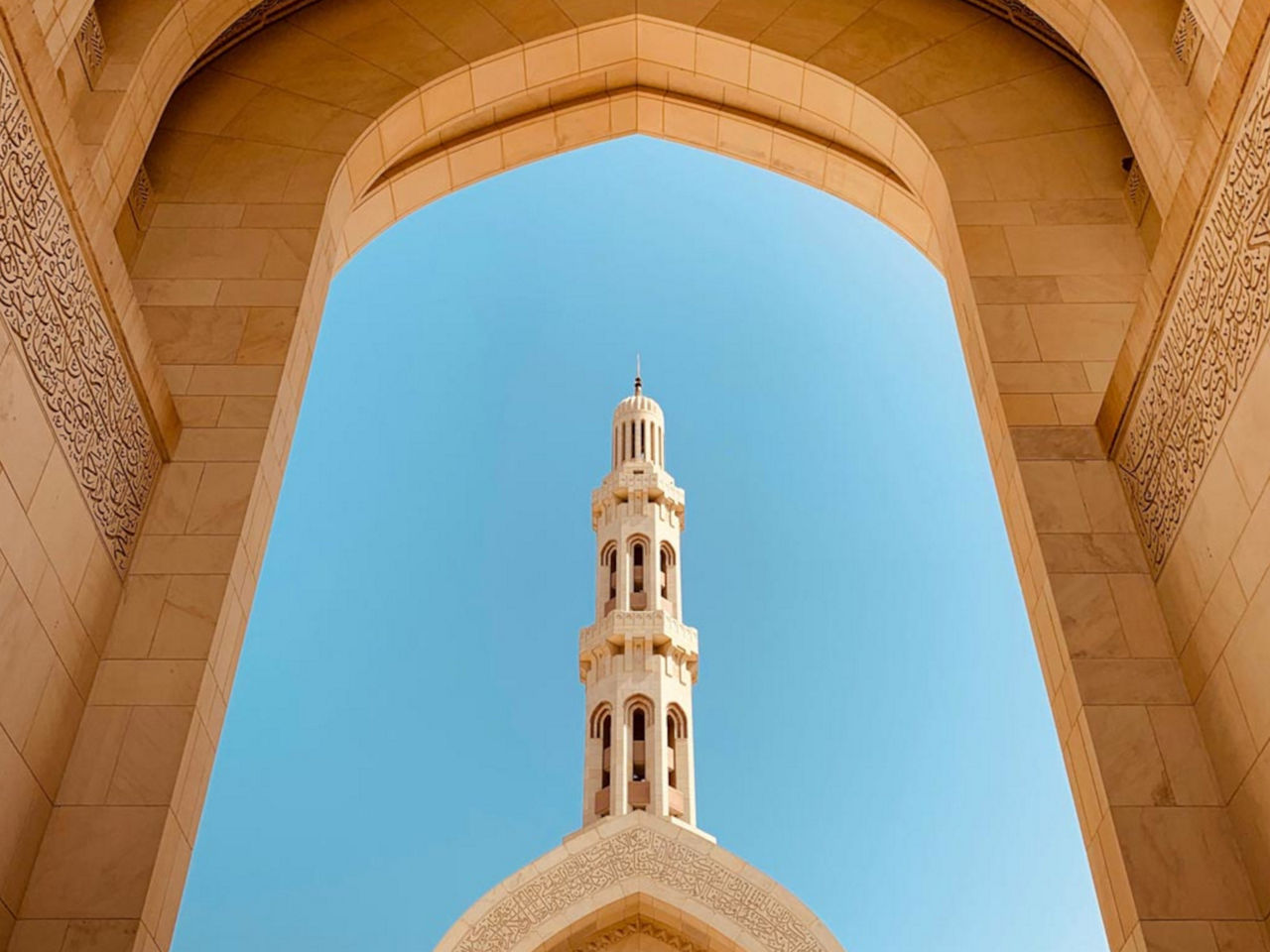 Minaret through the archway of a mosque against a blue sky.