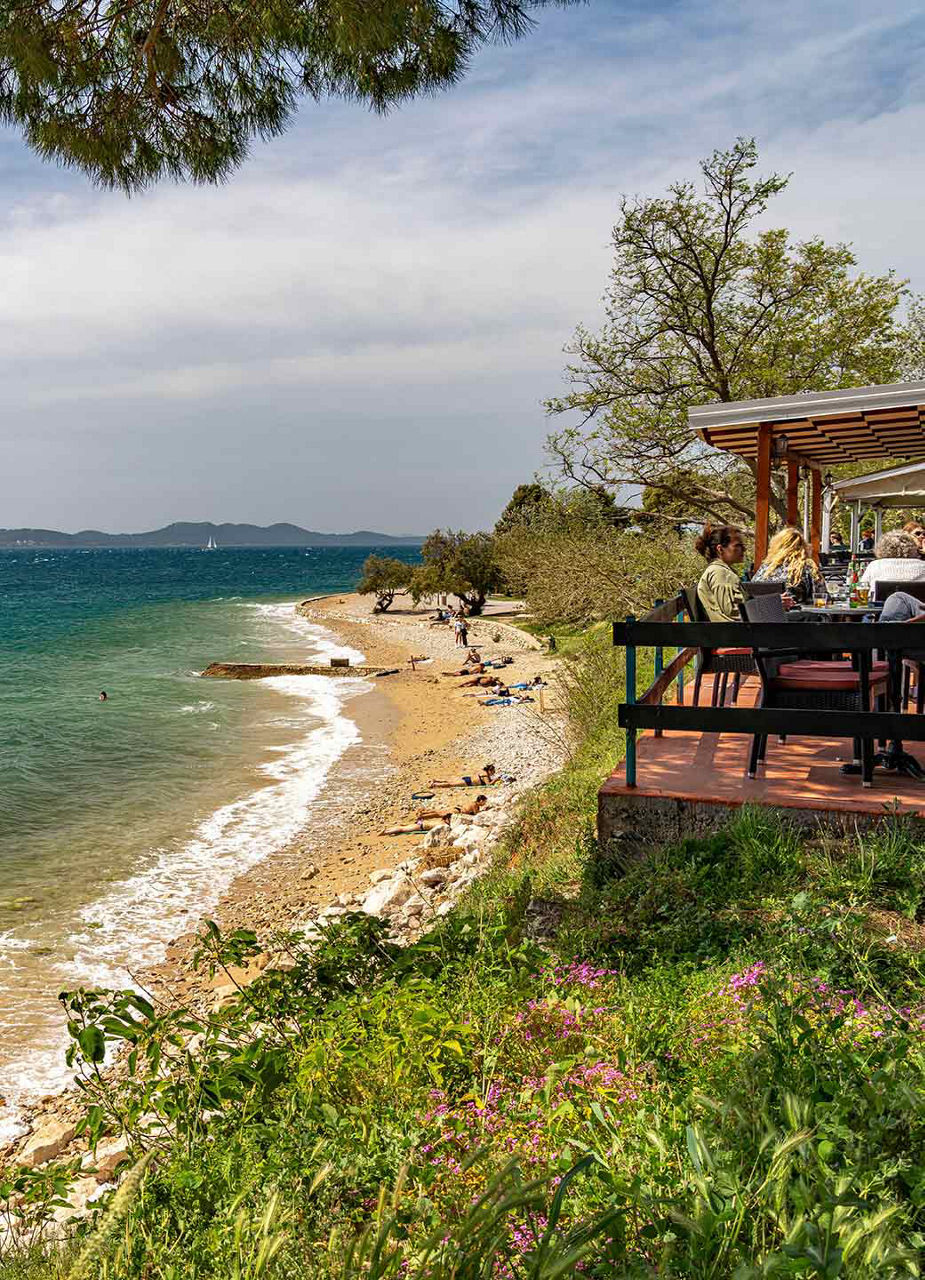Blick auf eine Restauranterrasse und den Strand von Kolovare